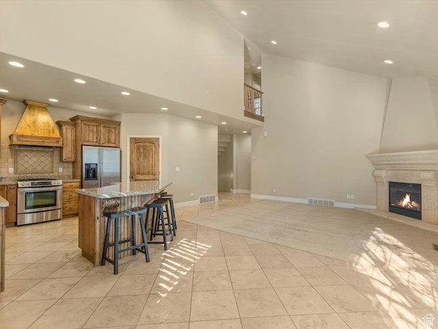 kitchen featuring custom exhaust hood, open floor plan, visible vents, brown cabinets, and appliances with stainless steel finishes