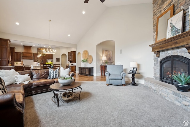 living room featuring ceiling fan with notable chandelier, high vaulted ceiling, a stone fireplace, arched walkways, and recessed lighting
