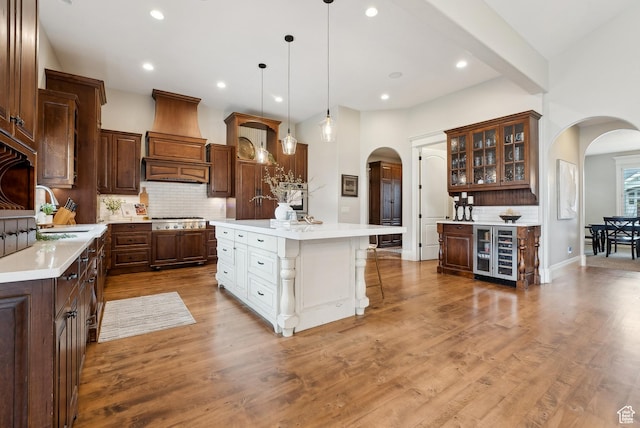 kitchen with wine cooler, stainless steel gas stovetop, a sink, premium range hood, and arched walkways