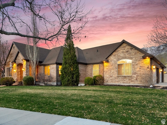 view of front facade featuring stone siding, a garage, a front lawn, a shingled roof, and brick siding