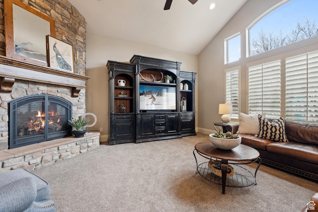 living room with a ceiling fan, baseboards, a stone fireplace, carpet flooring, and high vaulted ceiling