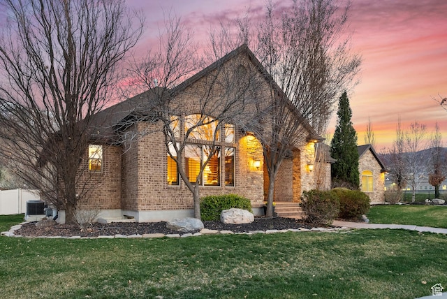 french country style house featuring cooling unit, brick siding, a front lawn, and fence