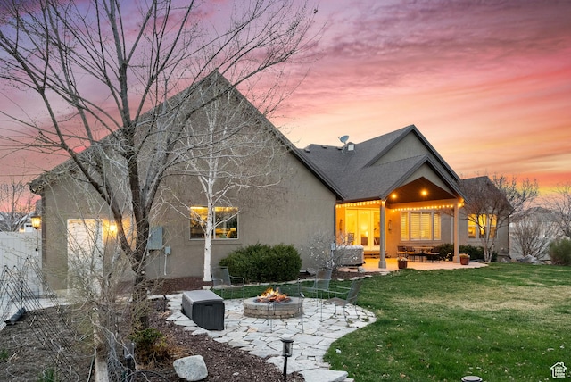 back of house featuring a yard, a patio area, stucco siding, and a fire pit