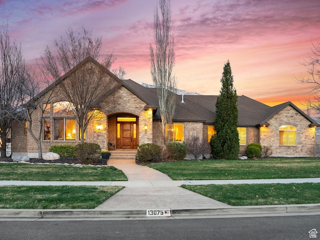 french country home featuring stone siding, brick siding, and a lawn