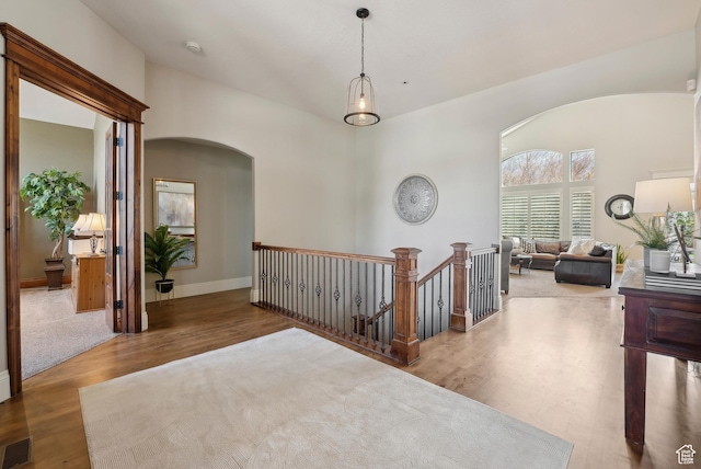 hallway with wood finished floors, a towering ceiling, visible vents, an upstairs landing, and arched walkways