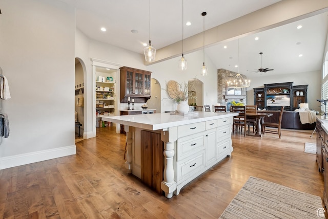 kitchen featuring a center island, arched walkways, light countertops, and glass insert cabinets