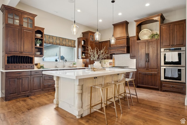 kitchen featuring a sink, wood finished floors, a breakfast bar, stainless steel double oven, and open shelves