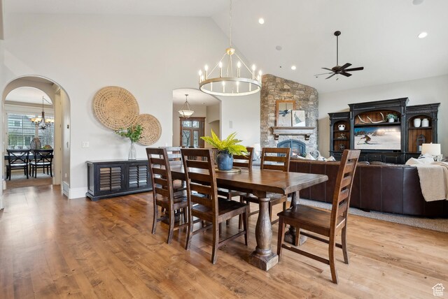 dining space featuring light wood finished floors, ceiling fan with notable chandelier, high vaulted ceiling, and arched walkways