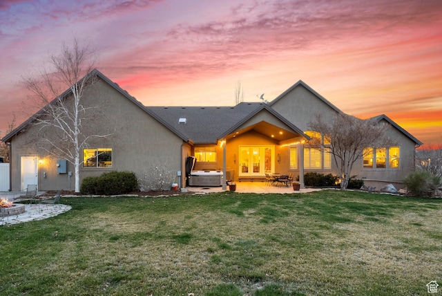 back of property with stucco siding, central air condition unit, a hot tub, a yard, and a patio area