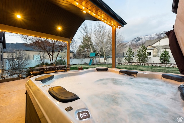 view of community featuring a mountain view, a playground, a lawn, a fenced backyard, and a patio area