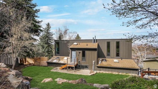 back of house with a shingled roof, board and batten siding, fence, and a lawn