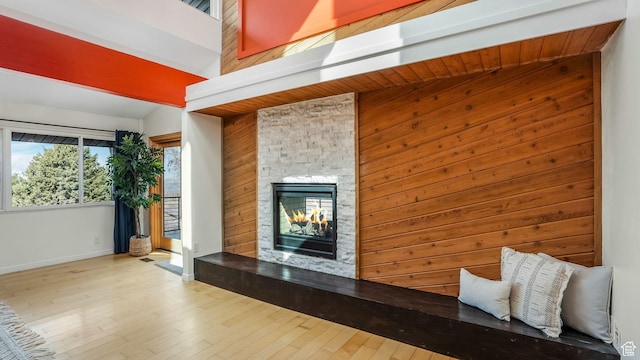 unfurnished living room with wooden walls, a stone fireplace, wood finished floors, and baseboards