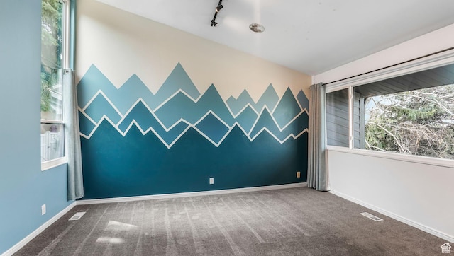 carpeted spare room with track lighting, baseboards, an accent wall, and visible vents