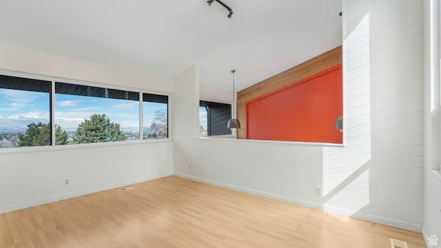 empty room with visible vents, baseboards, rail lighting, and wood finished floors