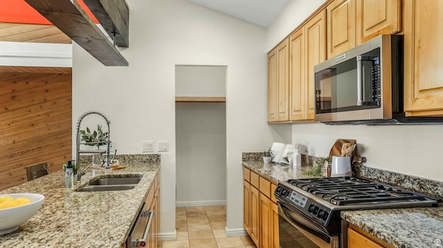 kitchen featuring light stone counters, stainless steel microwave, a sink, range with gas stovetop, and baseboards