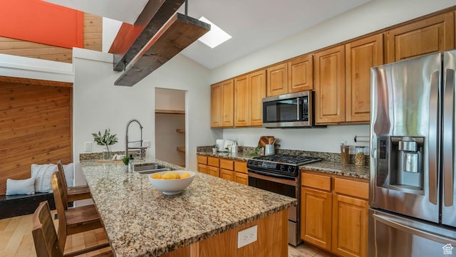 kitchen featuring vaulted ceiling with skylight, light stone counters, wood walls, a sink, and stainless steel appliances