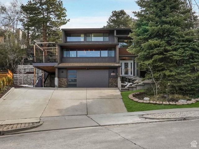view of front of house with a garage, stone siding, stairs, french doors, and concrete driveway