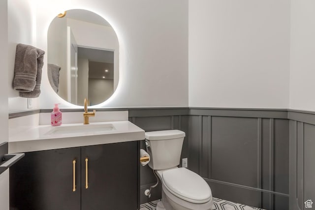 bathroom featuring a decorative wall, vanity, wainscoting, and toilet