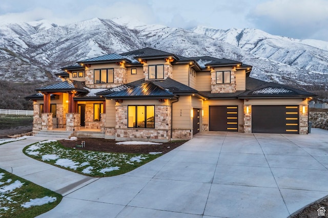prairie-style home with a garage, driveway, stone siding, and a mountain view