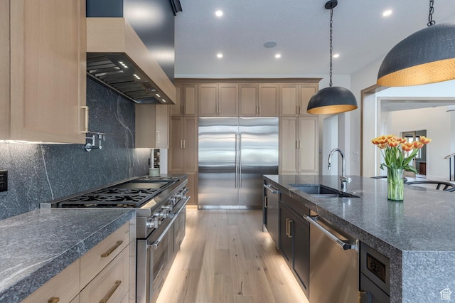 kitchen with custom range hood, high quality appliances, light wood-style floors, decorative backsplash, and a sink