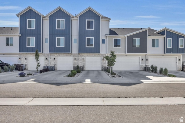 townhome / multi-family property with a garage, driveway, and stone siding