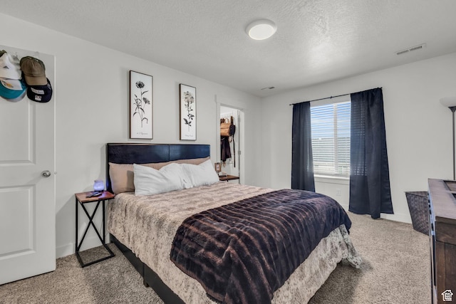bedroom featuring baseboards, a spacious closet, carpet flooring, a textured ceiling, and visible vents