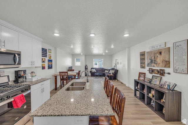 kitchen featuring an island with sink, light wood-style flooring, white cabinets, appliances with stainless steel finishes, and a sink