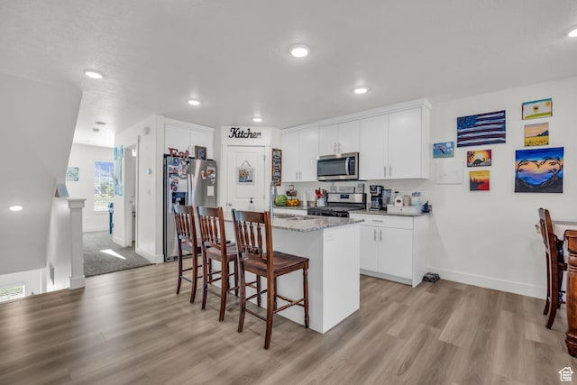 kitchen featuring a sink, appliances with stainless steel finishes, a kitchen bar, light wood-style flooring, and a kitchen island