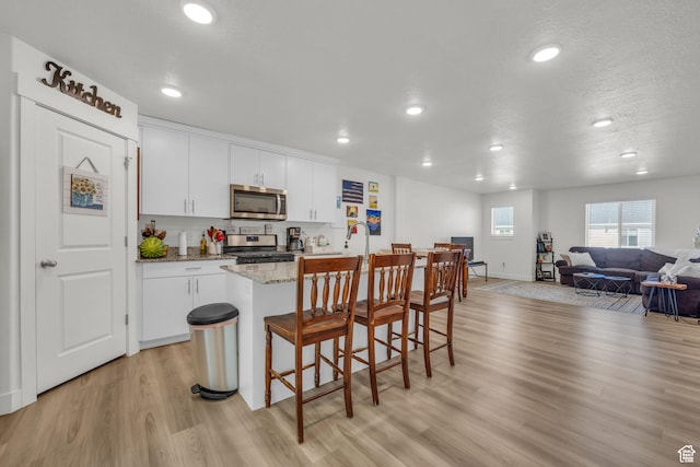 kitchen featuring light wood-style flooring, open floor plan, white cabinetry, and stainless steel appliances