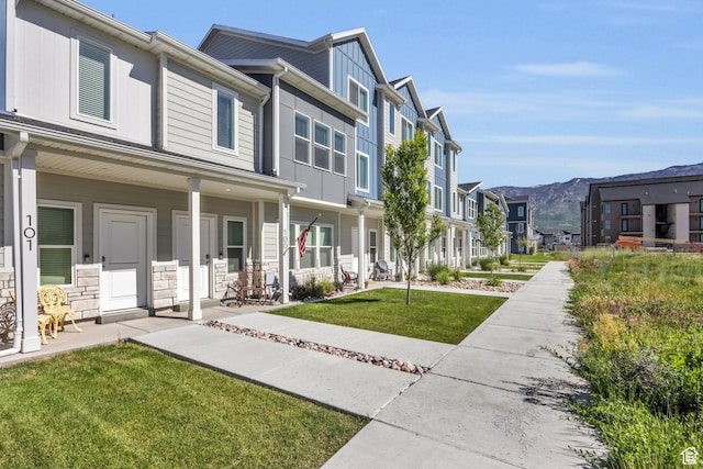 exterior space featuring covered porch, a front yard, stone siding, a mountain view, and a residential view