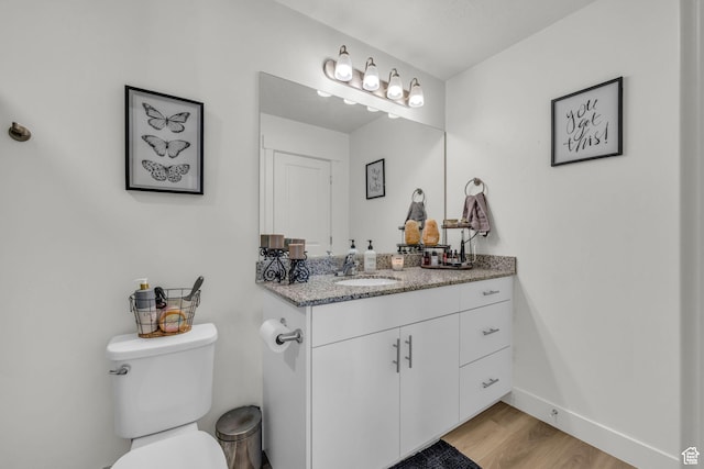 half bathroom with toilet, wood finished floors, vanity, and baseboards