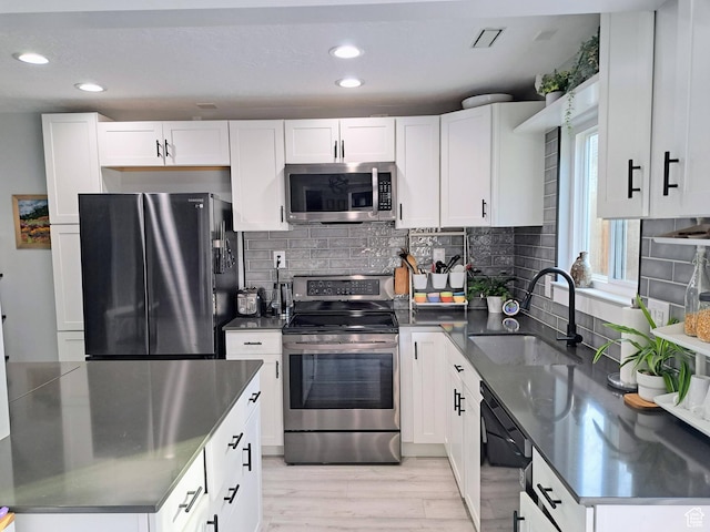 kitchen with tasteful backsplash, white cabinetry, appliances with stainless steel finishes, light wood finished floors, and a sink