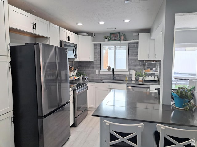 kitchen with a sink, dark countertops, a textured ceiling, stainless steel appliances, and backsplash