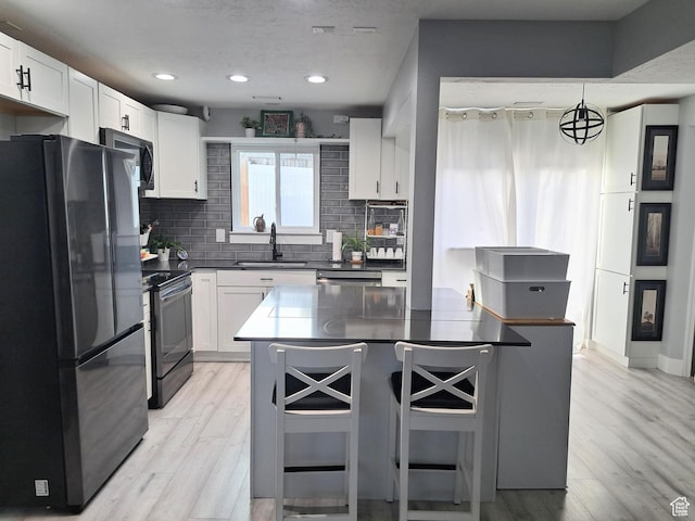 kitchen with freestanding refrigerator, a kitchen breakfast bar, a sink, dark countertops, and black range with electric cooktop