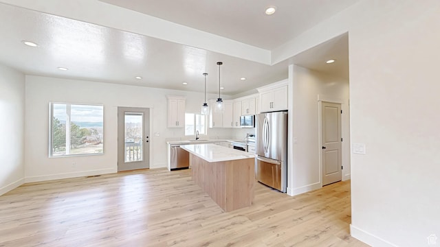 kitchen with light wood-type flooring, white cabinets, a center island, appliances with stainless steel finishes, and light countertops