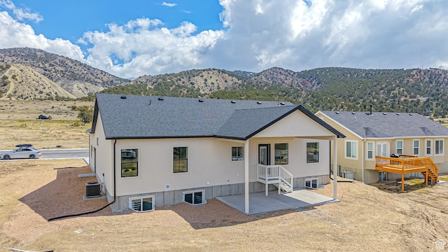 rear view of house featuring roof with shingles, stucco siding, a mountain view, a patio area, and central AC