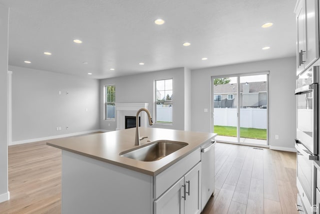 11888 S Golden Pine Ln, Riverton, UT 84065 - kitchen featuring a glass covered fireplace, light wood-type flooring, open floor plan, appliances with stainless steel finishes, and a sink