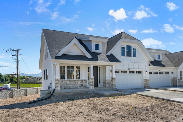 view of front of home featuring concrete driveway, roof with shingles, stone siding, a garage, and covered porch