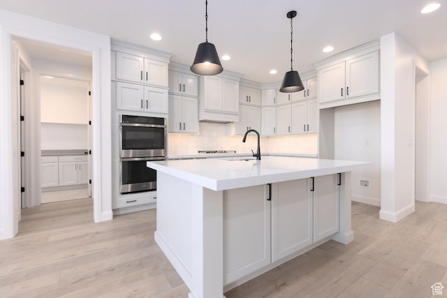 kitchen featuring double oven, light wood-style flooring, tasteful backsplash, a sink, and light countertops