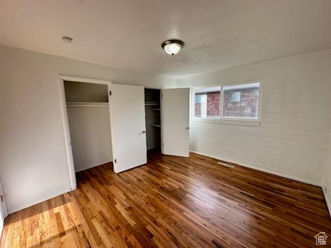 unfurnished bedroom featuring brick wall, two closets, and wood finished floors