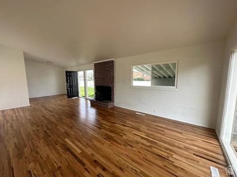 unfurnished living room featuring brick wall, a brick fireplace, and wood finished floors