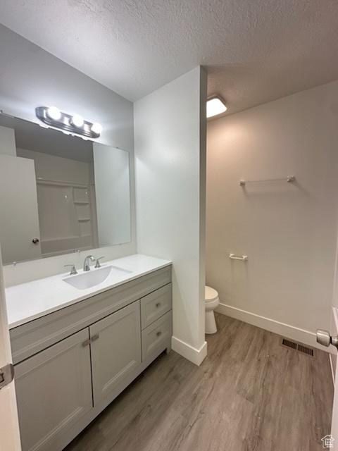 bathroom featuring a textured ceiling, vanity, visible vents, toilet, and wood finished floors