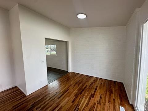 spare room featuring brick wall, visible vents, and wood finished floors