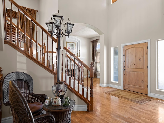 foyer featuring arched walkways, a high ceiling, wood finished floors, stairs, and baseboards