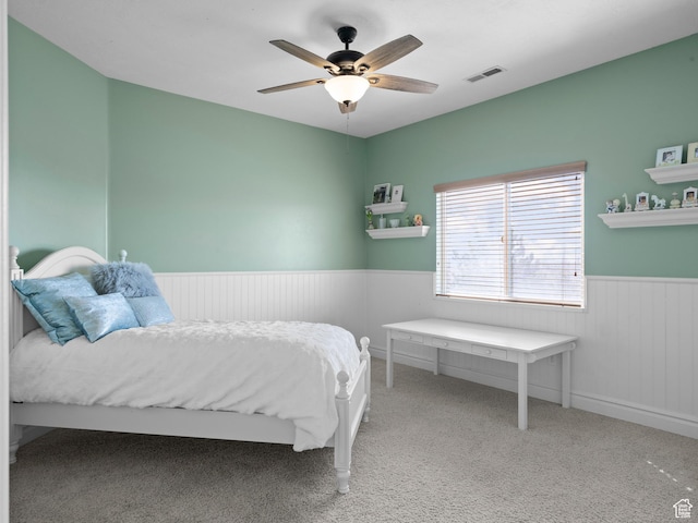 bedroom with a ceiling fan, carpet flooring, wainscoting, and visible vents