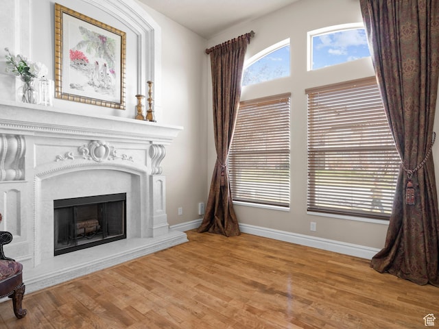 unfurnished living room featuring a fireplace with raised hearth, baseboards, and wood finished floors