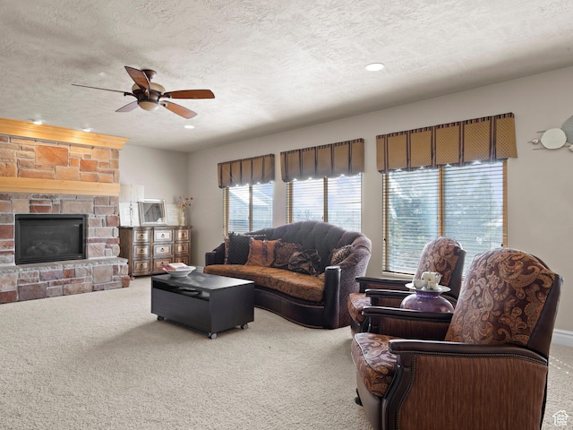 living area featuring a textured ceiling, ceiling fan, a stone fireplace, and carpet floors