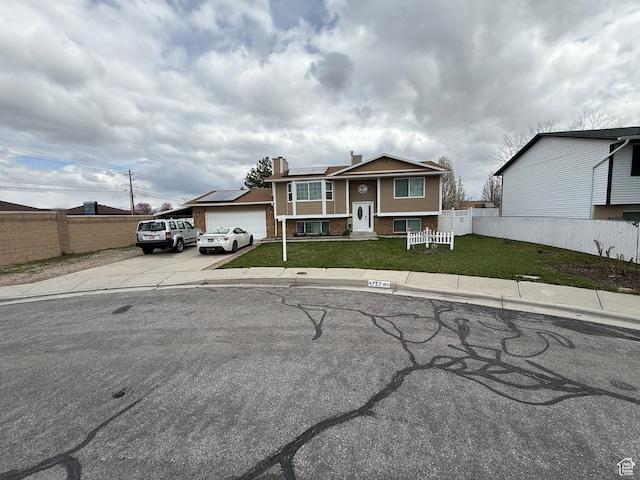 split foyer home featuring concrete driveway, fence, a front lawn, and roof mounted solar panels