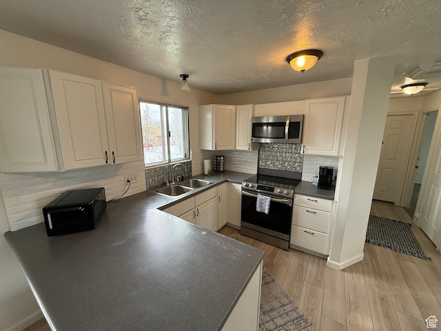 kitchen featuring white cabinets, a sink, light wood-type flooring, dark countertops, and stainless steel appliances