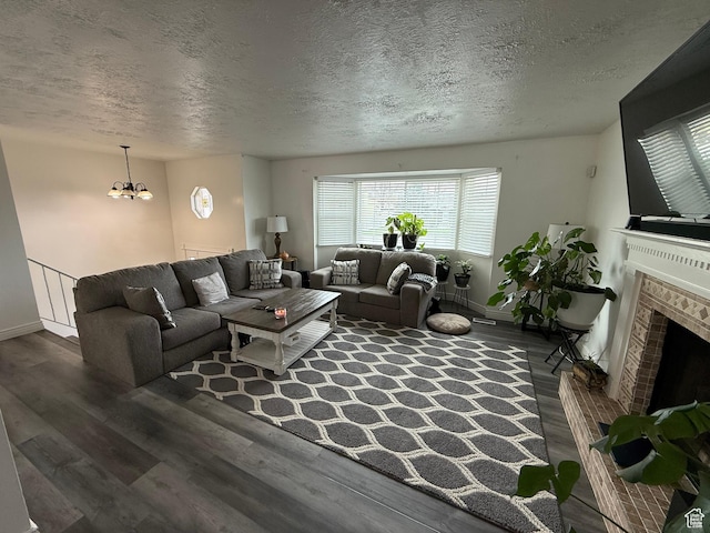 living room featuring a chandelier, a textured ceiling, wood finished floors, and a brick fireplace